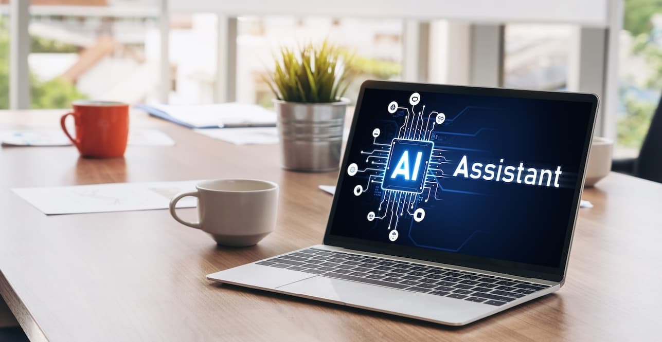 Laptop displaying "AI Assistant" on screen with circuit design, on wooden desk with coffee cups and small plant.